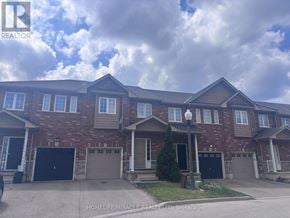 Hamilton (Lakeshore) townhouse for rent - A large brick house with a garage door and a tree in front.