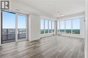 Kitchener condo for rent - A spacious room with wooden floors and large windows overlooking a cityscape.