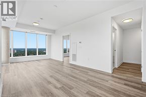 Kitchener condo for rent - A spacious room with wooden flooring and large windows overlooking a cityscape.