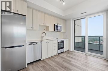 Kitchener condo for rent - A kitchen with white appliances and cabinets with a view of the city.