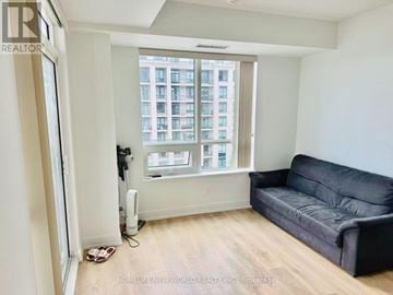 Markham (Unionville) condo for rent - A living room with a black couch and a window with a view of a building.