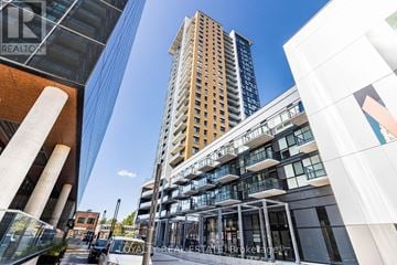 Kitchener condo for rent - A tall building with a glass facade stands in the middle of a city street.