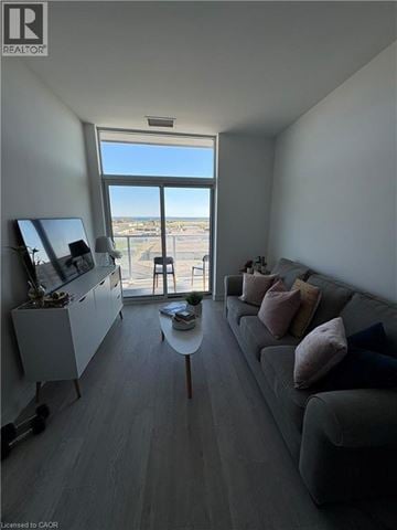 Hamilton condo for rent - A living room with a grey couch and a large window overlooking a parking lot.