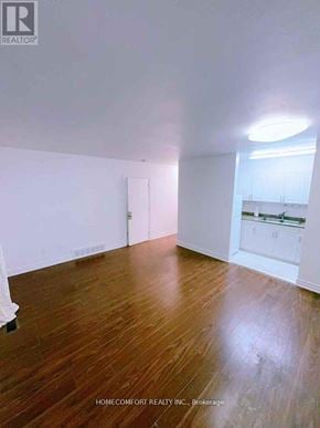 Toronto (Rexdale-Kipling) townhouse for rent - A room with wooden flooring and white walls, with a kitchen visible in the background.