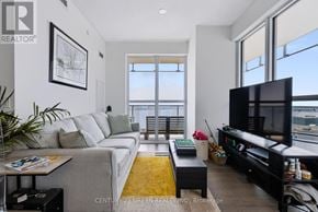 Toronto (Waterfront Communities) condo for rent - A living room with a grey couch, a coffee table, a flat screen TV and a large window.