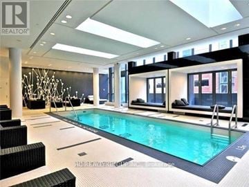 Toronto (Bay Street Corridor) condo for rent - A large indoor swimming pool with a black bench and a black chair.