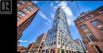 Toronto (Waterfront Communities) condo for rent - A tall building with many windows stands in the middle of a city street.