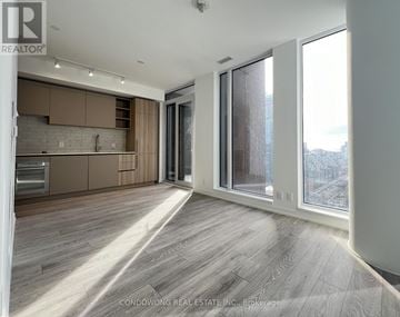Toronto (Waterfront Communities) condo for rent - A spacious room with wooden flooring and a kitchen area with a refrigerator, oven, and cabinets.