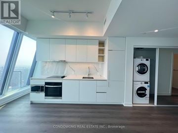 Toronto (Bay Street Corridor) condo for rent - A modern kitchen with white cabinets and appliances, with a view of the city outside the window.