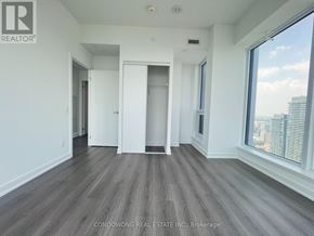Toronto (Bay Street Corridor) condo for rent - A spacious room with wood flooring and a large window overlooking a cityscape.