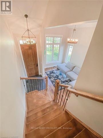 Fort Erie (Crystal Beach) apartment for rent - A staircase with a wooden handrail and a glass balustrade leads to a living room with a white couch and a chandelier.