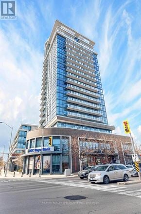 Mississauga (Port Credit) condo for rent - A tall building with a glass facade is situated in front of a street with cars and a traffic light.