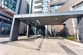 Mississauga (Port Credit) condo for rent - A modern building entrance with a covered walkway and a sign for RE/MAX Realty Specialists of the Block.