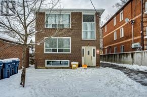 Toronto (Rockcliffe-Smythe) multi-family for rent - A snow-covered ground in front of a brick building with a sign that says RE/MAX Realty Specialists Brokerage.