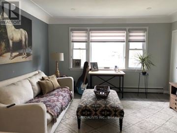 Burlington (Brant) multi-family for rent - A woman is standing in a living room with a couch, a table, and a painting of a horse on the wall.