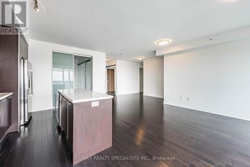 Toronto (Bay Street Corridor) condo for rent - A spacious room with wooden floors and white walls, featuring a kitchen area with dark wood cabinets and a white countertop.