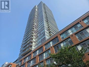 Toronto (Waterfront Communities) condo for rent - A tall building with many windows is seen in the foreground with a clear blue sky in the background.