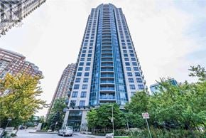 Mississauga (City Centre) condo for rent - A tall building with many windows is surrounded by trees.