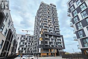 Oakville (Jm Joshua Meadows) condo for rent - A tall residential building with balconies and windows is surrounded by other buildings.