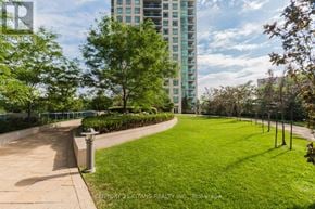 Mississauga (City Centre) condo for rent - A grassy park area with a walkway and a tall building in the background.