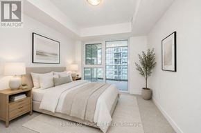 Pickering (Bay Ridges) condo for rent - A bedroom with a large bed, a nightstand with a lamp, a potted plant, and pictures on the wall.