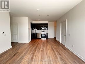Pickering (Bay Ridges) condo for rent - A spacious room with wooden flooring and a kitchen area in the background.