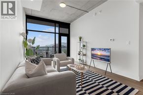 Hamilton apartment for rent - A living room with a grey sofa, a black and white striped rug, a wooden coffee table, and a large window with a view of the city.