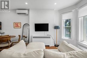 Toronto (Roncesvalles) multi-family for rent - A living room with a white couch and a flat screen TV mounted on the wall.