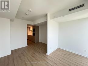 Toronto (Moss Park) condo for rent - A spacious room with wood flooring and white walls, featuring a ceiling light and a small wooden cabinet with a mirror above it.