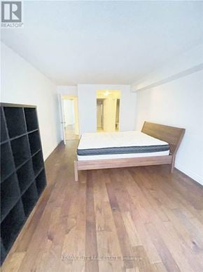 Toronto (Bay Street Corridor) condo for rent - A bedroom with a bed, wooden floors, and a black bookshelf.