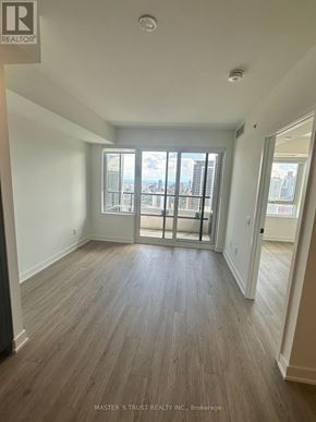 Toronto (North St. James Town) condo for rent - A room with wooden flooring and a large window overlooking a cityscape.