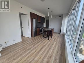 Toronto (University) condo for rent - A spacious room with wooden flooring and a kitchen area with a bar stool.