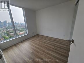 Toronto (University) condo for rent - A room with wooden flooring and a large window overlooking a cityscape.