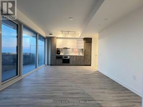 Toronto (Waterfront Communities) condo for rent - A spacious room with wooden flooring and a kitchen area in the background.