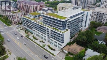 Toronto (Bayview Village) condo for rent - A modern building with a green roof is surrounded by other buildings and a road with cars.