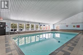 Cobourg condo for rent - A large indoor swimming pool with a tiled floor and a glass wall on one side.
