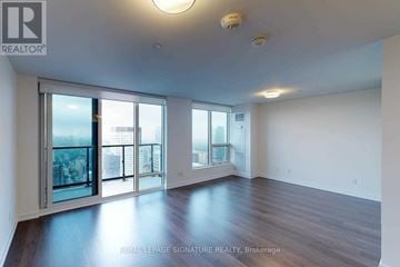 Toronto (Mount Pleasant West) condo for rent - A spacious room with wooden floors and large windows overlooking a cityscape.