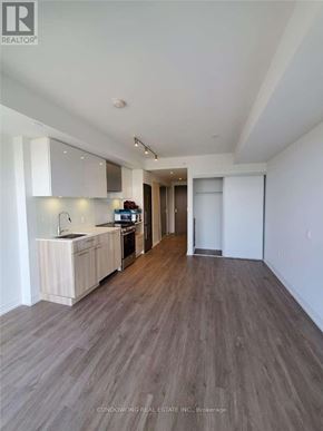 Toronto (Moss Park) condo for rent - A spacious room with wooden flooring and a kitchen area with white cabinets and appliances.
