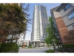Surrey apartment for rent - A tall, modern glass building stands next to a smaller brick building with a tree in front.