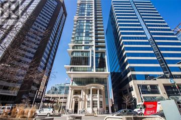 Toronto (University) condo for rent - A tall building with a white entrance sits between two modern skyscrapers.