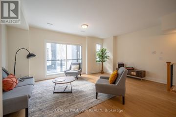 Orillia townhouse for rent - A living room with a grey couch, a black floor lamp, and a small table with a plant on it.