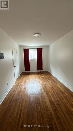 Toronto (Cliffcrest) fourplex for rent - A room with wooden floors and a window with red curtains.