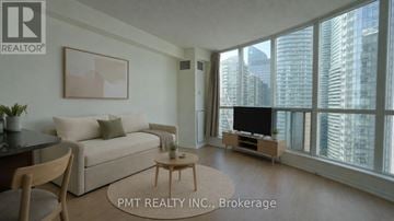 Toronto (Waterfront Communities) condo for rent - A living room with a couch, a coffee table, and a television with a city view through the windows.