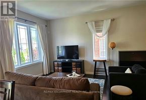 Grimsby (Grimsby Beach) townhouse for rent - A living room with a brown couch, a black chair, and a television.
