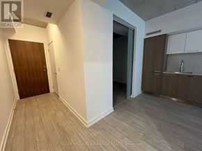 Toronto (South Riverdale) condo for rent - A room with a wooden door and a kitchen area with brown cabinets.