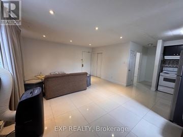 Mississauga (Port Credit) multi-family for rent - A spacious living room with a brown sofa and a kitchen area in the background.