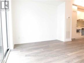 Toronto (Waterfront Communities) condo for rent - A large empty room with wooden flooring and a kitchen area in the background.