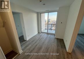 Toronto (Downsview-Roding-Cfb) condo for rent - A spacious room with wooden flooring and a view of the city through the sliding glass door.