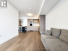 Toronto (Bay Street Corridor) condo for rent - A spacious living room with a grey couch and a kitchen area in the background.