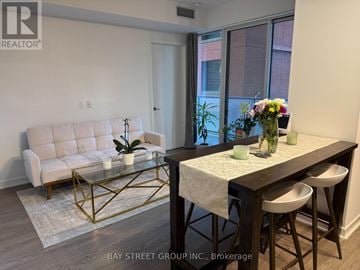 Toronto (Waterfront Communities) condo for rent - A living room with a white couch, a glass coffee table, and a dining table with chairs.